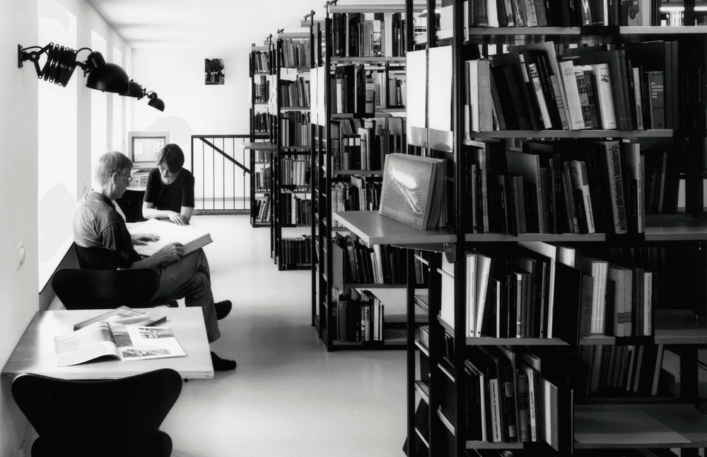 Der Blick in die Bibliothek zeigt zwei lesende Personen und gefüllte Bücherregale.