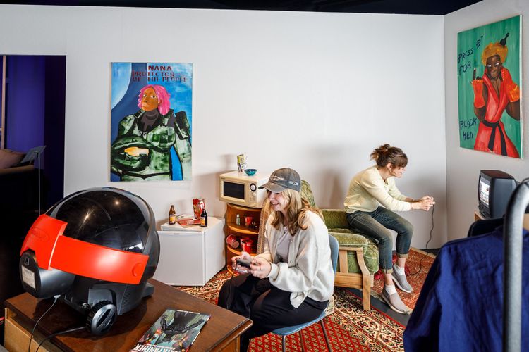Installationsansicht auf Larry Achiampongs Jugendzimmer mit zwei Personen, die jeweils vor einem Monitor sitzen und mit Konsolen spielen. 